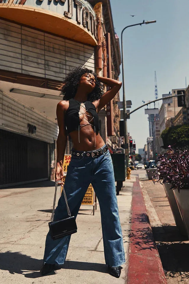 Woman posing in a black cropped top with a lace-up rhinestone front and jeans outdoors