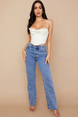 Full body shot of a woman in a white satin corset top and blue jeans