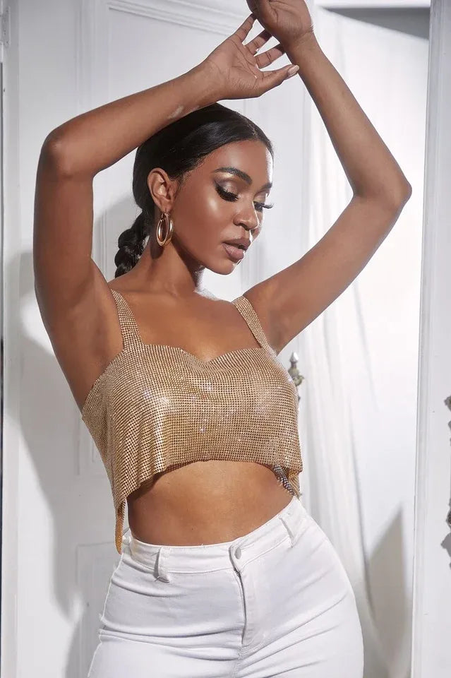 Woman with arms raised, wearing a gold rhinestone crop top and white pants