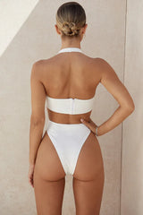 Rear view of woman in white one-piece swimsuit with halter neckline and high-cut leg.