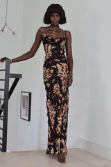 Woman wearing a black floral print maxi slip dress with spaghetti straps and a cowl neck, standing on a staircase.