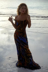 Woman wearing a black, blue, orange, and yellow abstract print maxi dress with spaghetti straps, standing on a beach.