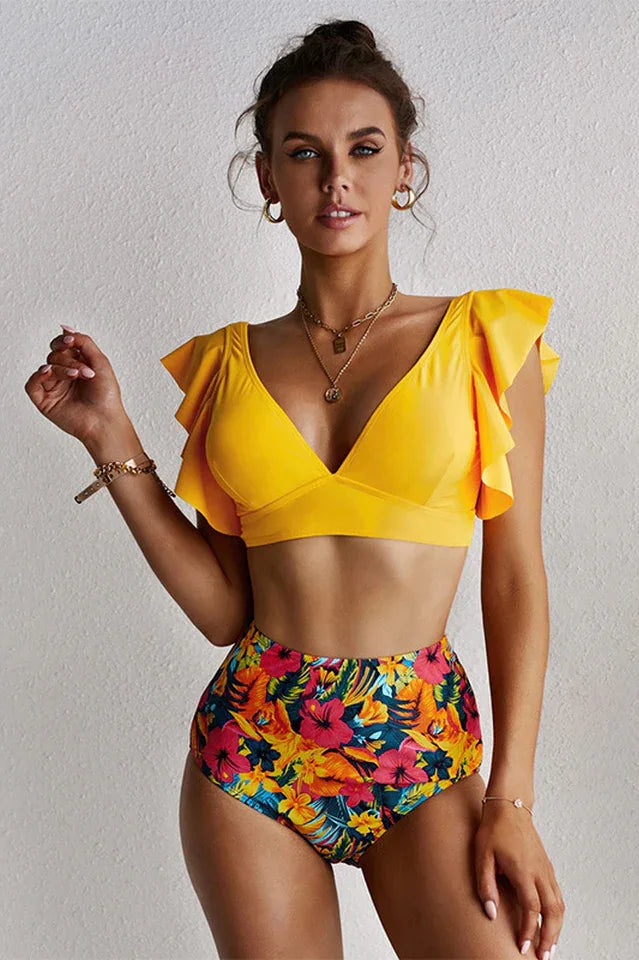 Woman wearing a yellow v-neck bikini top with flutter sleeves and tropical floral high-waisted bottoms