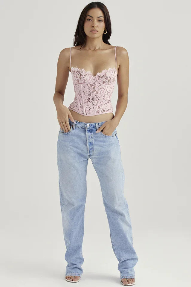 Full body shot of a woman in a pink lace corset top and light wash denim jeans, standing against a white background.