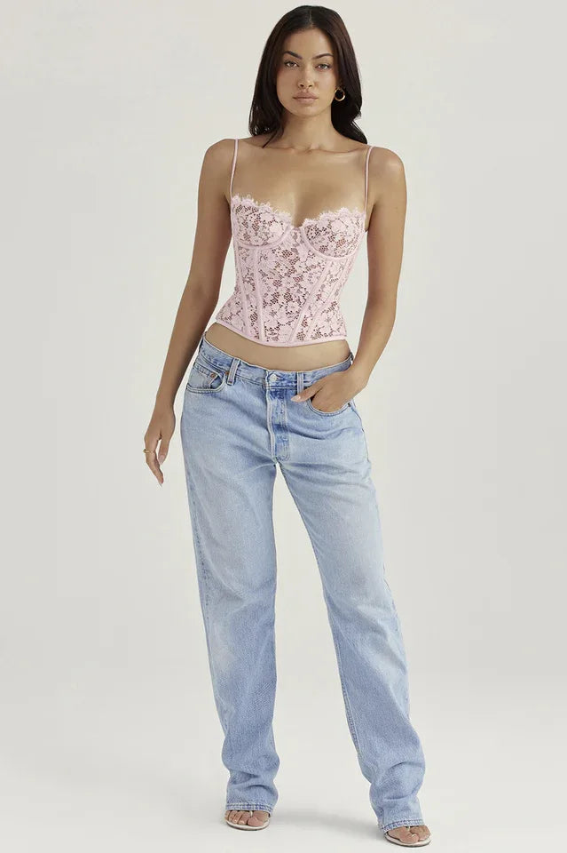 Woman posing in a pink lace corset top and light wash denim jeans, with hands in pockets.