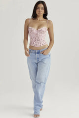 Woman wearing a pink lace corset top and light wash denim jeans, facing forward.