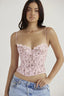 Woman wearing a pink lace corset top with spaghetti straps and light wash denim jeans.