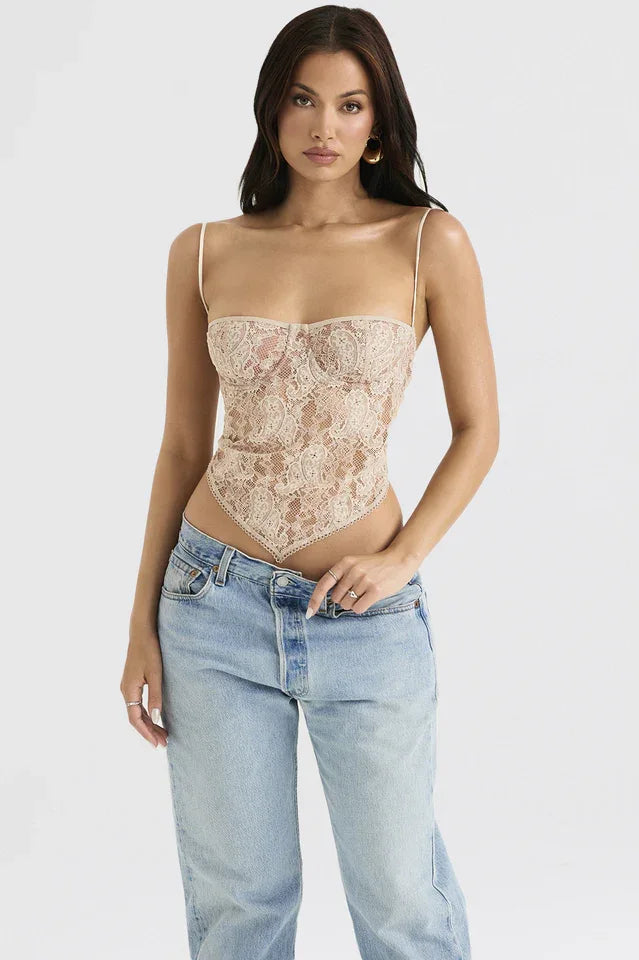 Woman modeling a beige lace corset top with a scarf hem and spaghetti straps, paired with light-wash denim jeans.