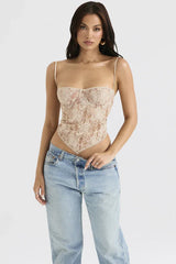 Woman modeling a beige lace corset top with a scarf hem and spaghetti straps, paired with light-wash denim jeans.
