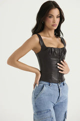 Side view of a woman wearing a dark brown faux leather corset top with a square neckline and hook and eye front closure, paired with light wash denim cargo pants.