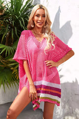 Woman wearing a bright pink crocheted cover-up with a striped hem, posing with her hand on her hip.
