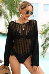 Woman wearing a black crochet knit cover-up over a black bikini and sunglasses, holding a straw hat by a pool with palm trees.