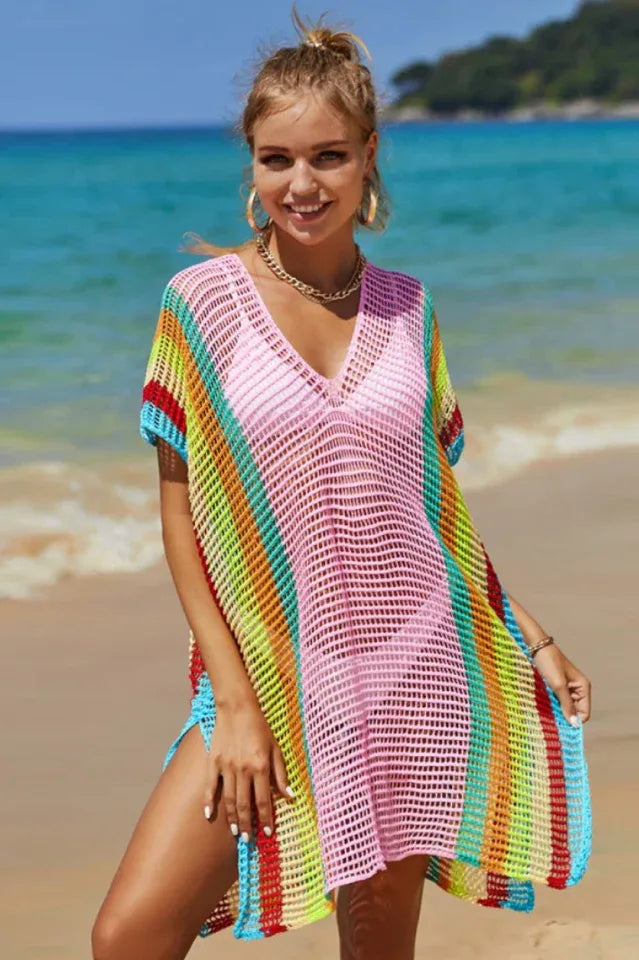Woman wearing a pink beach cover-up with colorful stripes and a pink bikini on the beach.