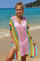 Woman wearing a pink beach cover-up with colorful stripes and a pink bikini on the beach.