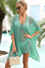 Woman wearing a green crocheted knit poncho cover-up with a v-neck, short sleeves, and sunglasses, holding a woven bag.