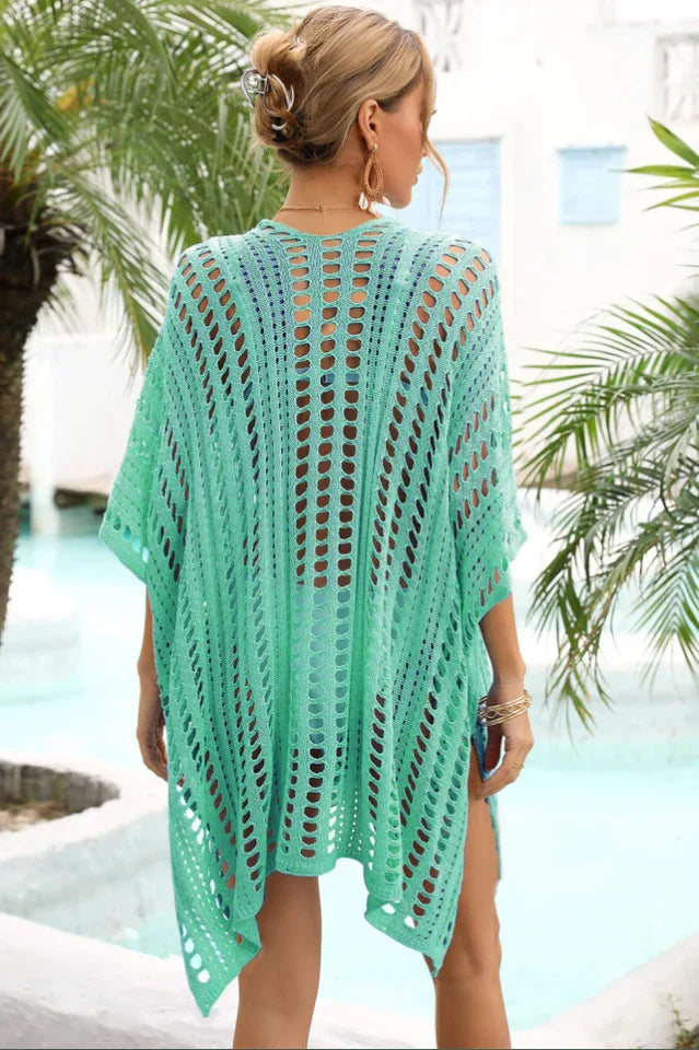 Back view of a woman wearing a green crocheted knit poncho cover-up with a v-neck and short sleeves.