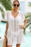 Woman wearing a white crochet knit tunic cover-up with a v-neckline and short sleeves, holding a straw hat.