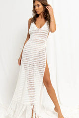 Woman wearing a white crocheted maxi dress with a high slit and fringe hem, viewed from the front.