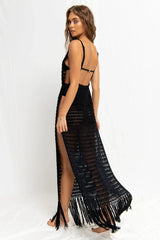Woman wearing a black crocheted maxi dress with a high slit and fringe hem, viewed from the back.