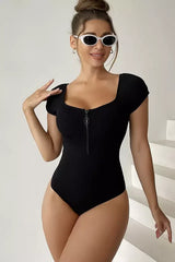 Woman wearing a black ribbed knit one-piece swimsuit with short sleeves and a zipper closure, posing.