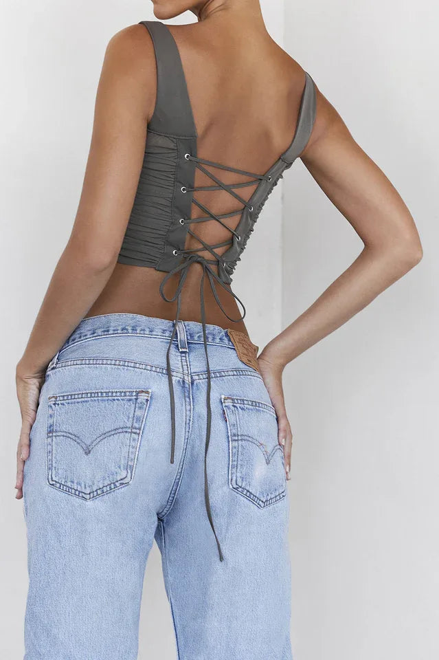 Back view of a woman wearing a khaki ruched corset top with a lace-up back detail and denim jeans.