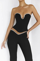 Close-up front view of a woman's torso wearing a black strapless corset top with crystal trim and matching black high-waisted pants with crystal trim.