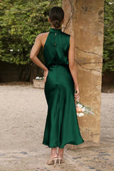 back view of a woman wearing a green satin halter neck midi dress outdoors