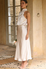 Side view of a woman wearing a champagne satin halter neck midi dress, standing near a door frame.