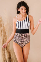Front view of a woman wearing a one-piece swimsuit with a stripe and leopard print design, with her arms slightly extended