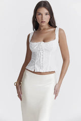 Full body shot of a woman in a white embroidered eyelet sleeveless square neck top and a white satin midi skirt.