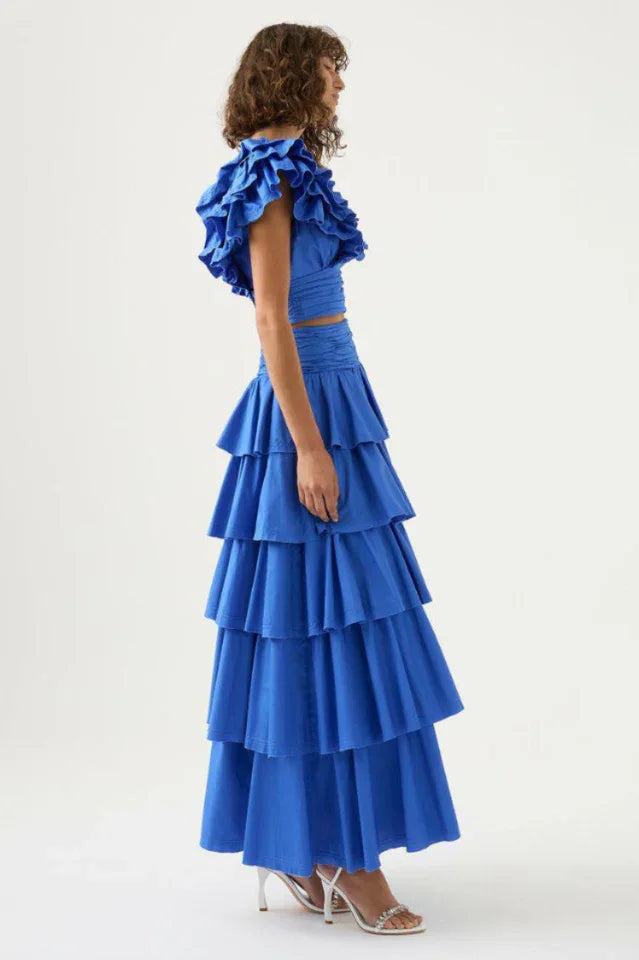 Side view of a woman in a blue ruffled crop top and tiered blue maxi skirt