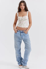 Full body shot of a woman wearing a white floral print corset top and light wash, relaxed fit denim jeans.