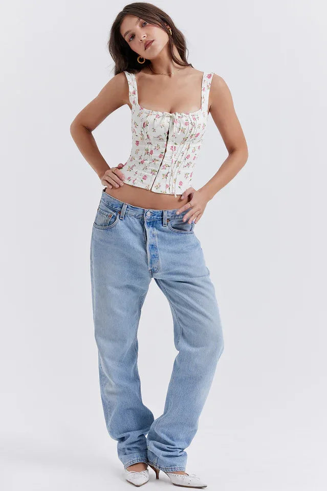 Woman with hands in pockets, wearing a white floral print corset top and light wash denim jeans, showcasing the outfit.