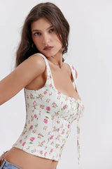 Close-up of a woman wearing a white floral print corset top with pink roses, highlighting the sweetheart neckline and tie front detail.