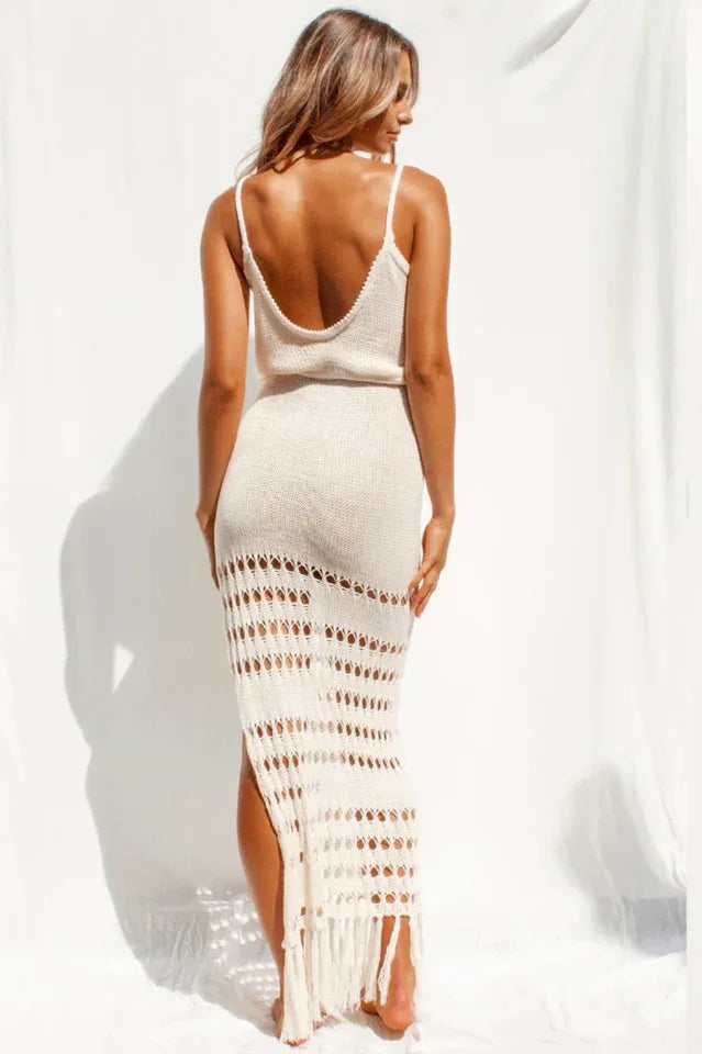 Rear view of a woman in a cream knitted maxi dress with crochet detailing and a high slit.