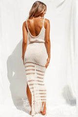 Rear view of a woman in a cream knitted maxi dress with crochet detailing and a high slit.