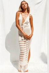 Woman wearing a cream knitted maxi dress with a deep v-neck and a tie waist, standing against a white backdrop.