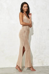 Side view of a woman in a beige knit maxi dress with a high slit.