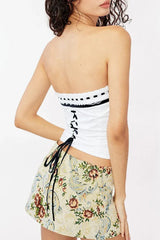 Close-up of a woman's back wearing a white strapless top with black trim and lace-up detail.