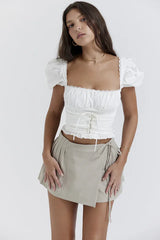 Full body shot of a woman wearing a white cropped puff sleeve top and a beige wrap skirt.