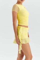 side view of a woman in a yellow ruched mesh mini dress