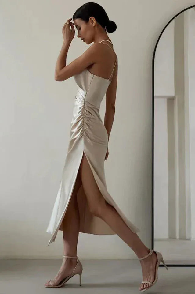 Side view of a woman in a champagne satin slip dress with a cowl neckline and high slit, walking.