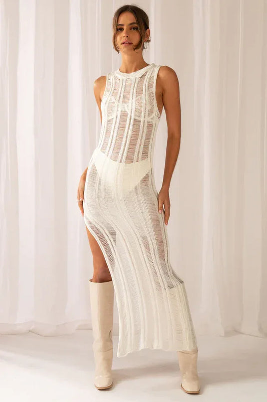 Woman wearing a white sleeveless maxi dress with a high slit and a sheer knit construction, paired with cream boots.
