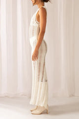 Profile view of a woman wearing a white sleeveless maxi dress with a high slit and sheer knit construction, with cream boots.
