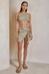 Woman wearing a light gold crochet knit halter top and a matching mini skirt with a tie closure.