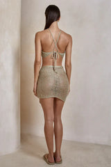Back view of a woman in a light gold crochet knit halter top and a matching mini skirt.