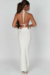 Back view of a woman wearing a white crochet knit halter neck bikini top and a matching white crochet knit high-waisted maxi skirt with cut-out details and tie closures.