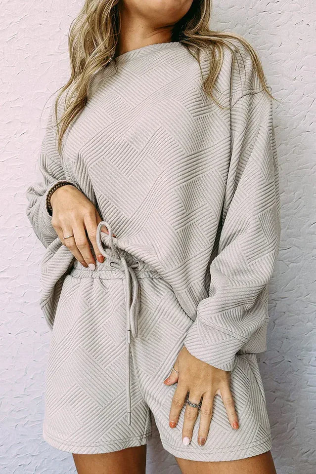 Close-up of a woman wearing a light beige textured knit long-sleeve top and matching shorts.