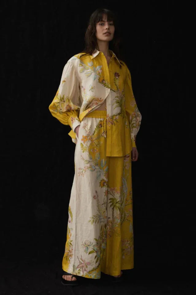 Woman wearing a yellow and cream floral print linen shirt and wide leg pants.