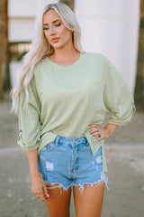 Woman wearing a light green ribbed crew neck top with rolled sleeves and distressed denim shorts.